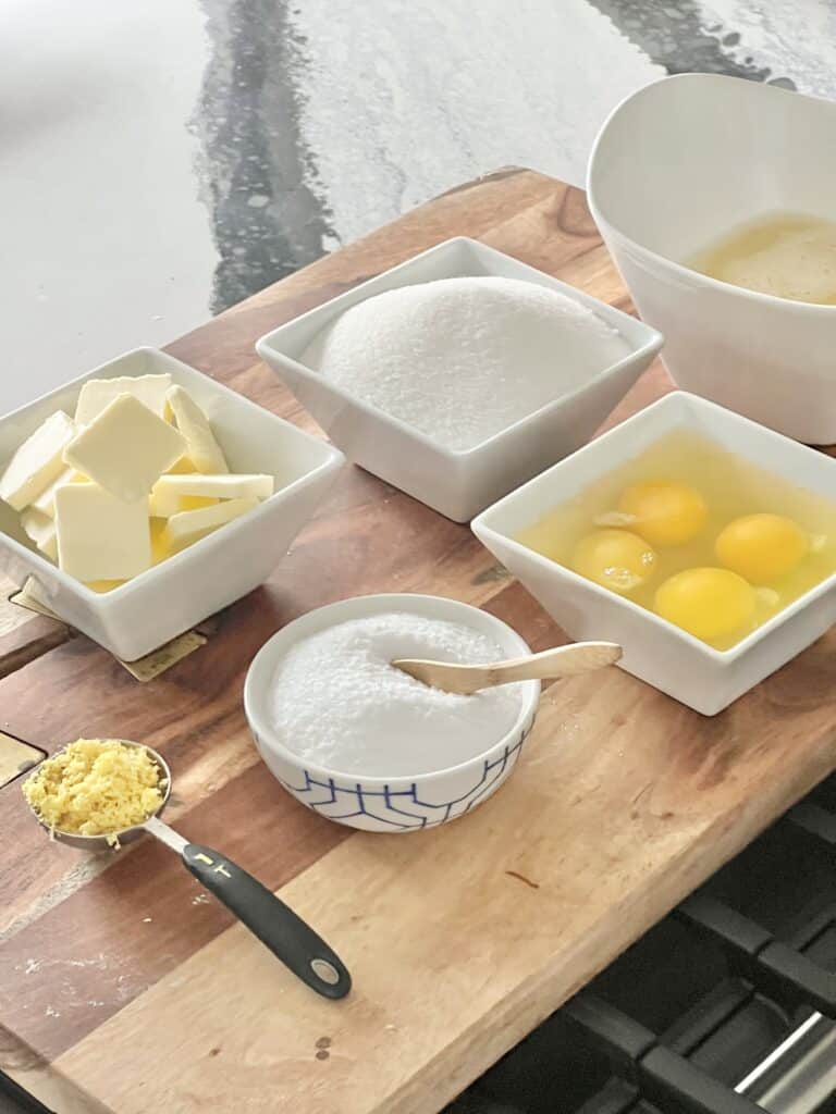 Ingredients for lemon curd displayed on a wood cutting board.