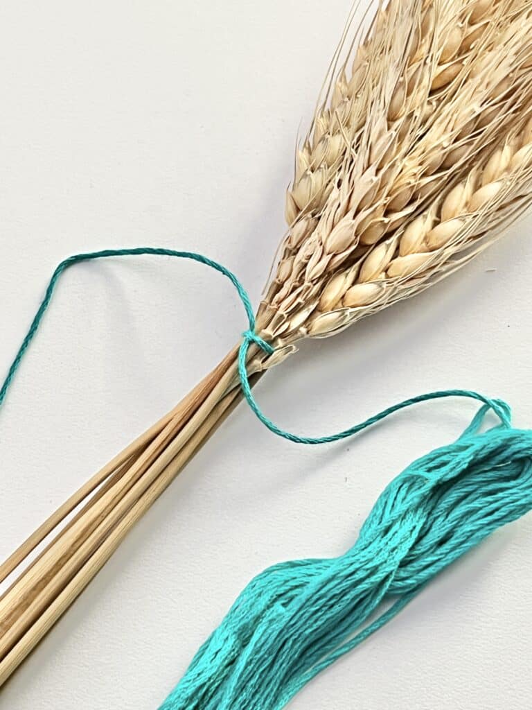 Teal embroidery thread tied in a knot at the base of the wheat.