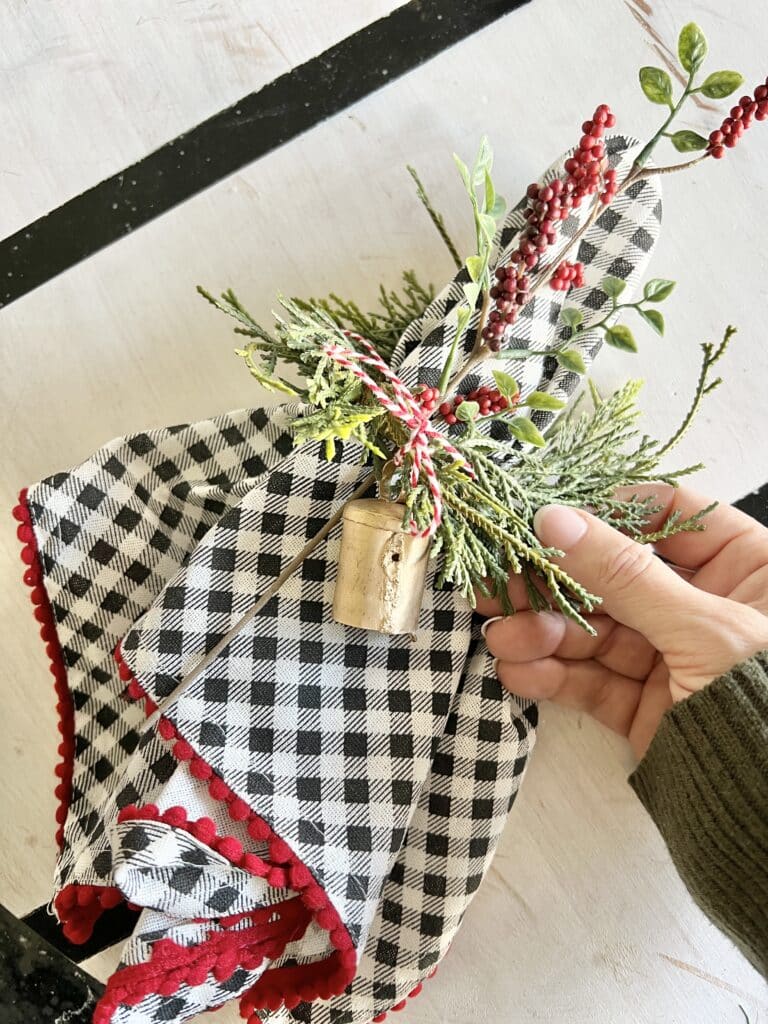 A napkin with a cedar napkin ring, brass bell, and winterberries.