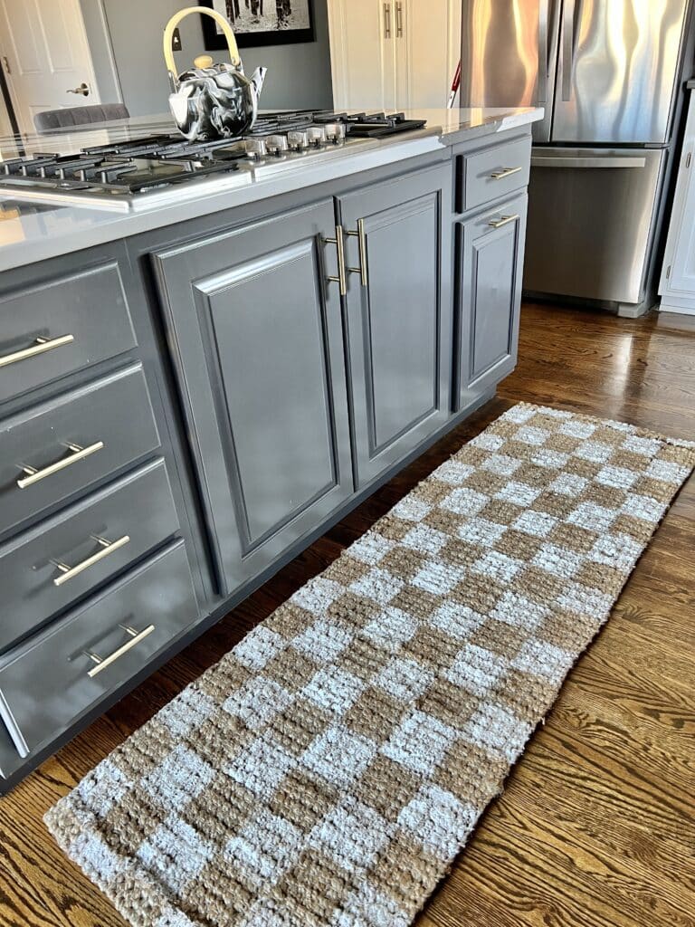 The checkerboard jute rug laying in front of the cooktop.