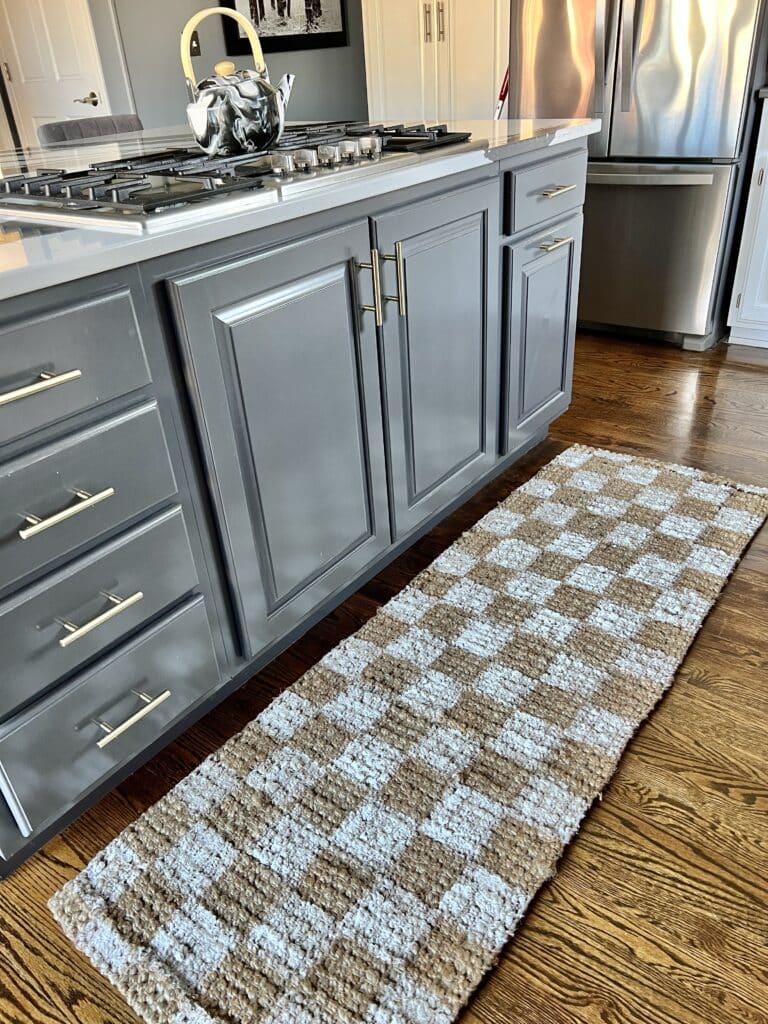 A checkered jute rug laying in front of a kitchen island stovetop.