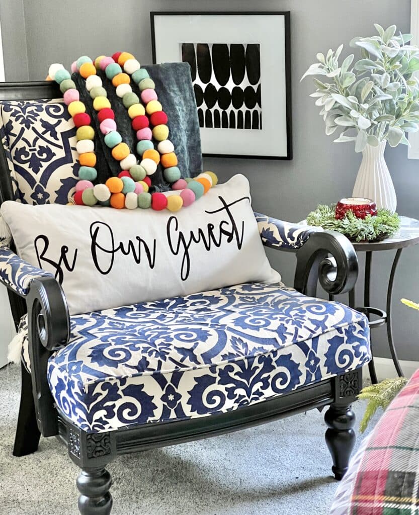 A blue and white chair with a pillow that says "Be Our Guest"