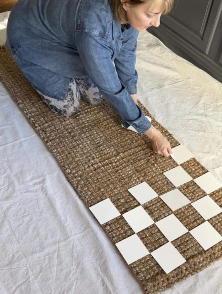 Woman laying poster board squares in a checkerboard pattern on the  rug to create the pattern for the painted jute rug.