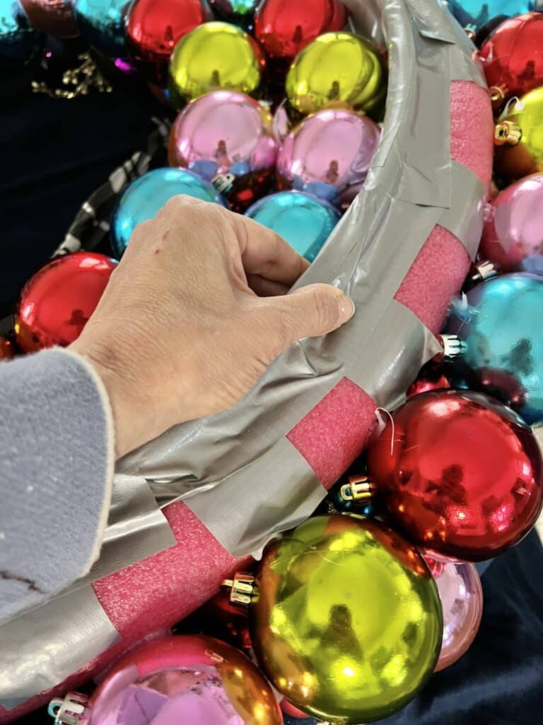 Attaching a hula hoop to the back of the pool noodle ornament wreath with duct tape.