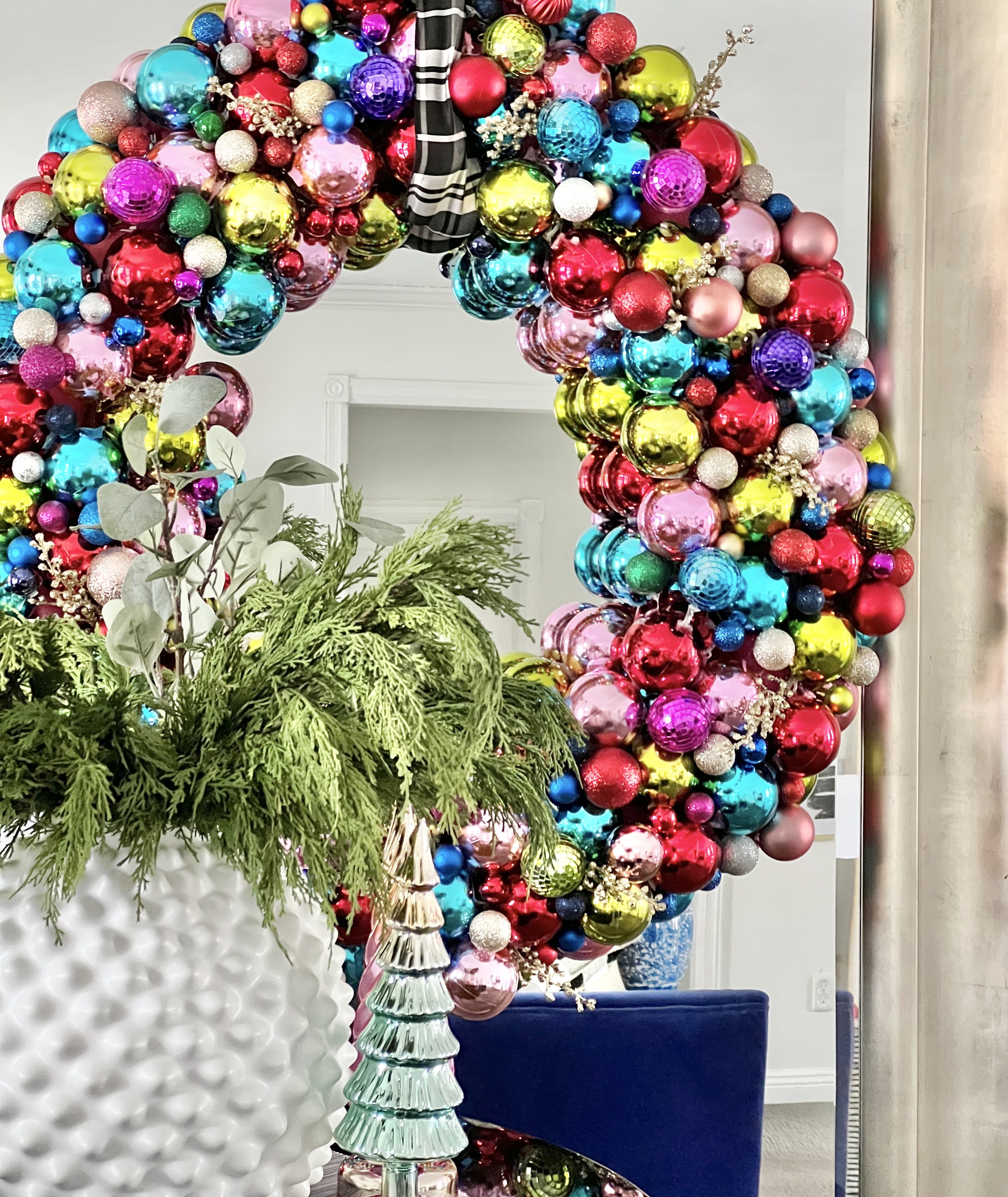 A pool noodle Christmas ornament wreath hanging on the front of a large mirror.