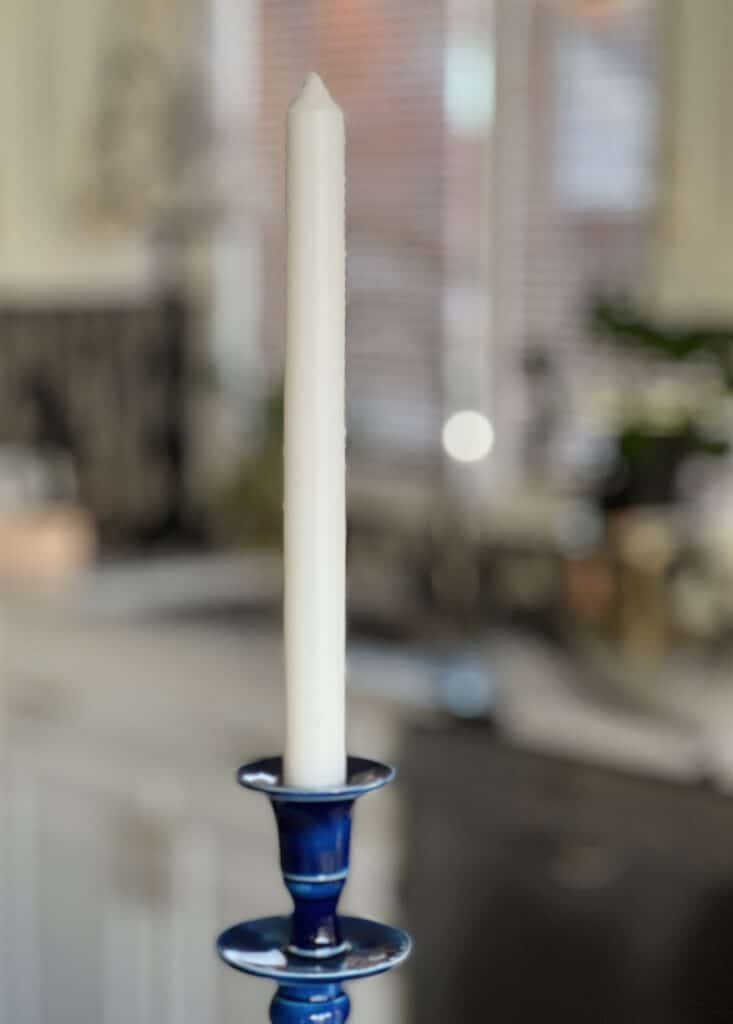 A single cream colored taper candle in a blue candlestick.