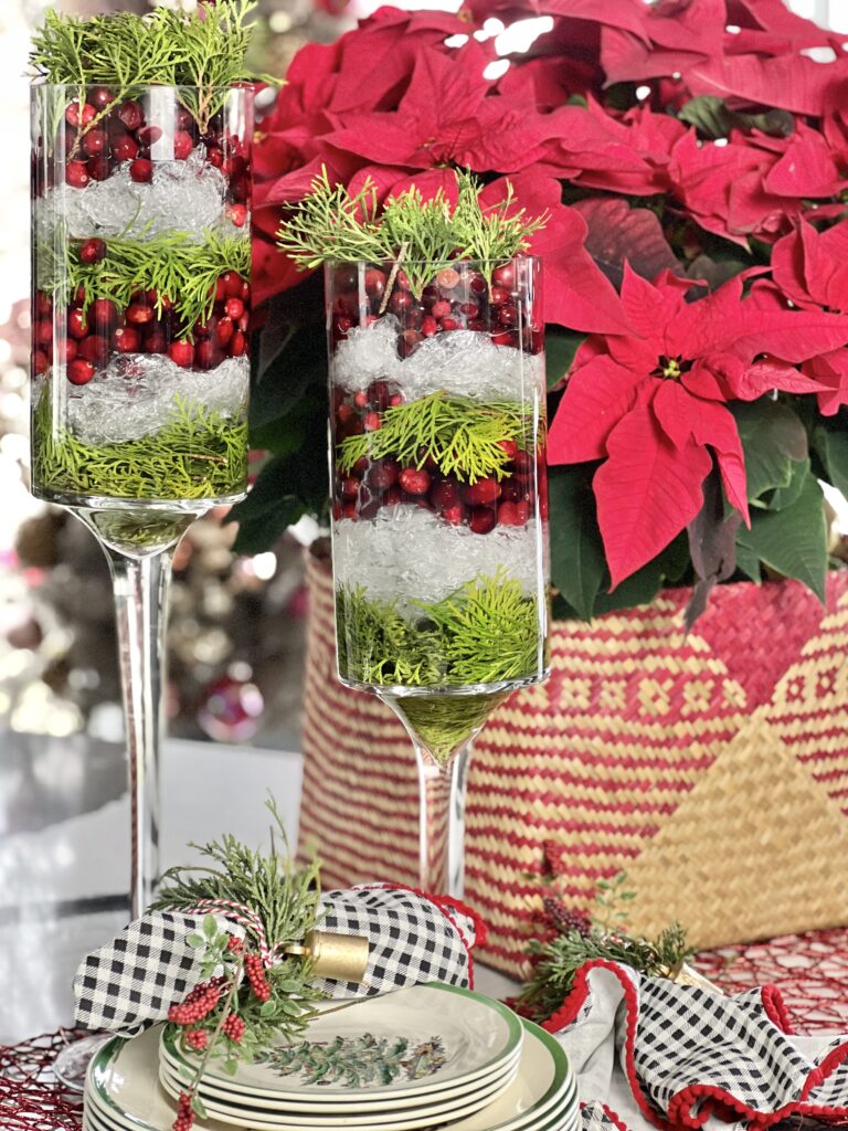An icy evergreen cranberry Christmas centerpiece sitting beside a poinsettia plant.