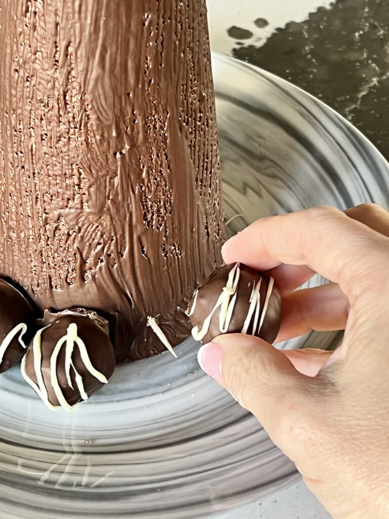 Placing Christmas truffle recipe balls onto a toothpick on a styrofoam cone.