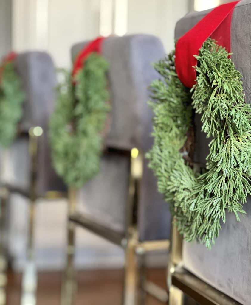 Green wreaths hanging from kitchen counter stools.