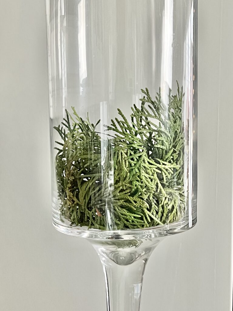 A glass container with fresh evergreen cuttings.