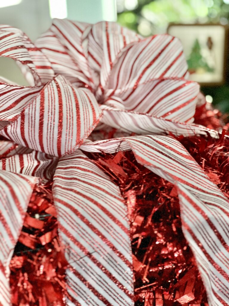 A large red and white stripe box sitting on top of the tinsel Christmas present.