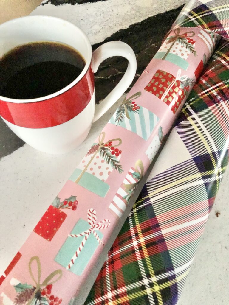 A cup of coffee beside some colorful Christmas wrapping paper.