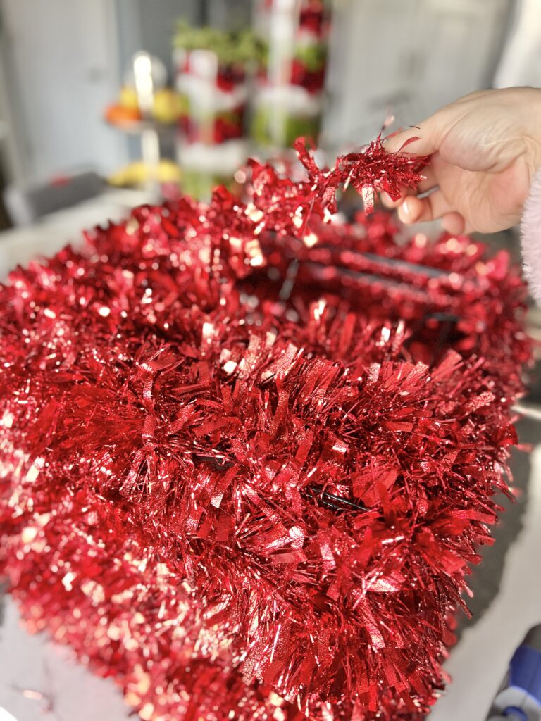 Weaving red tinsel garland to cover the top of the Christmas gift present.