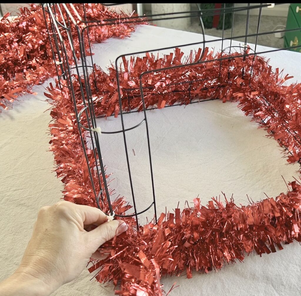 Wrapping red tinsel around the base of the square wreath frame.