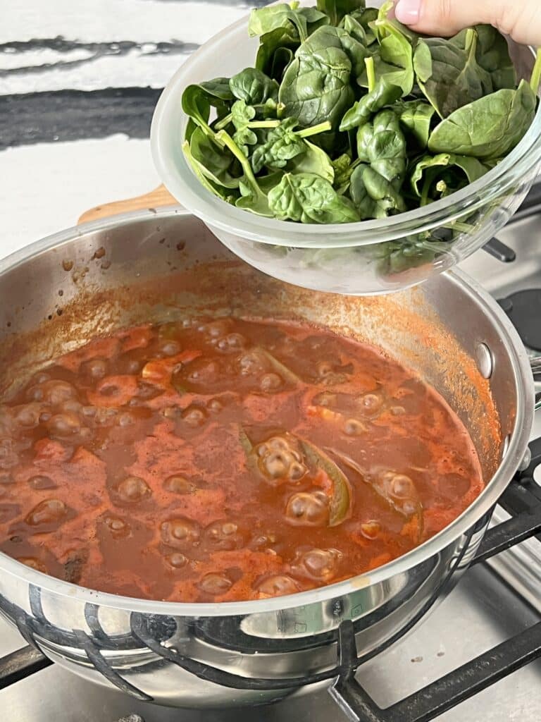 Pouring a bowl of fresh spinach into a simmering pot of healthy winter vegetable soup.