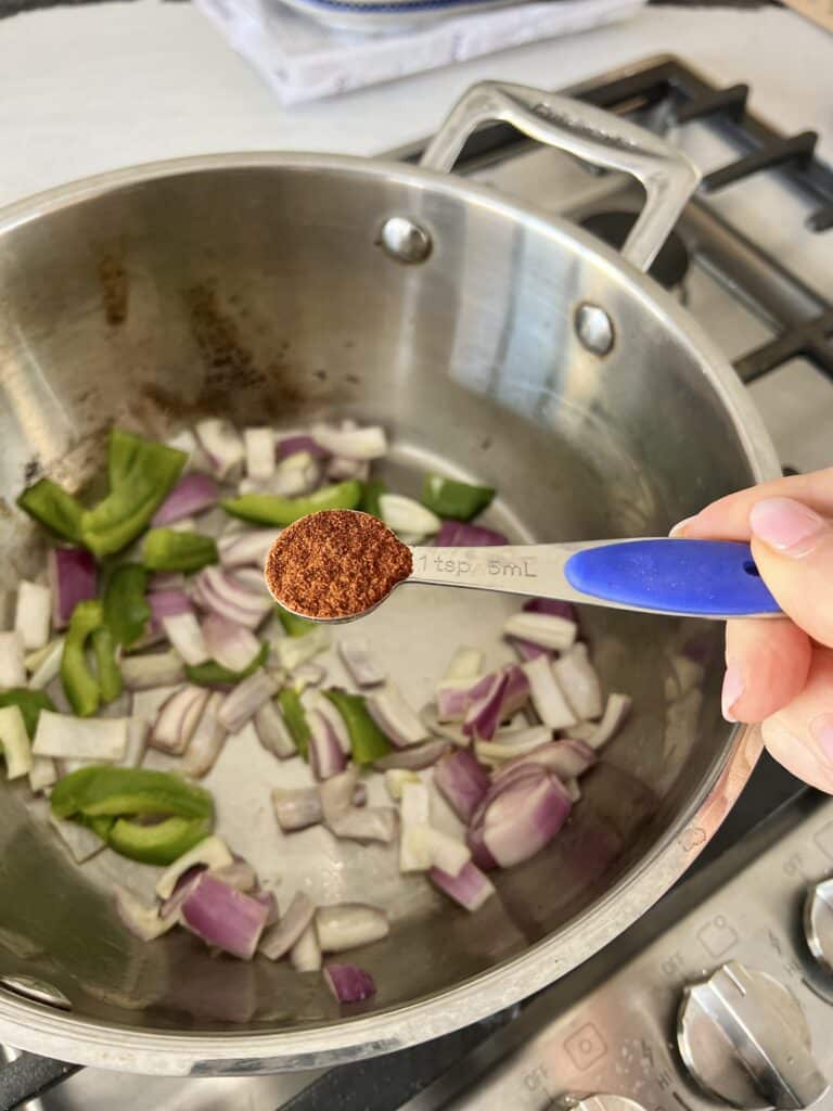 Adding chili powder to a pot of green papers and onions.