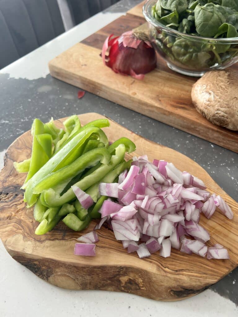 Chopped green peppers and onions on a wood cutting board.