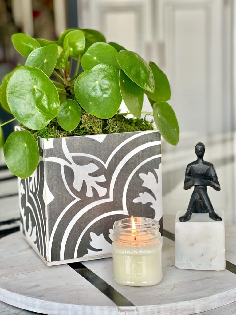 The completed DIY tile planter holding a green plant and styled with a small sculpture and jar candle.