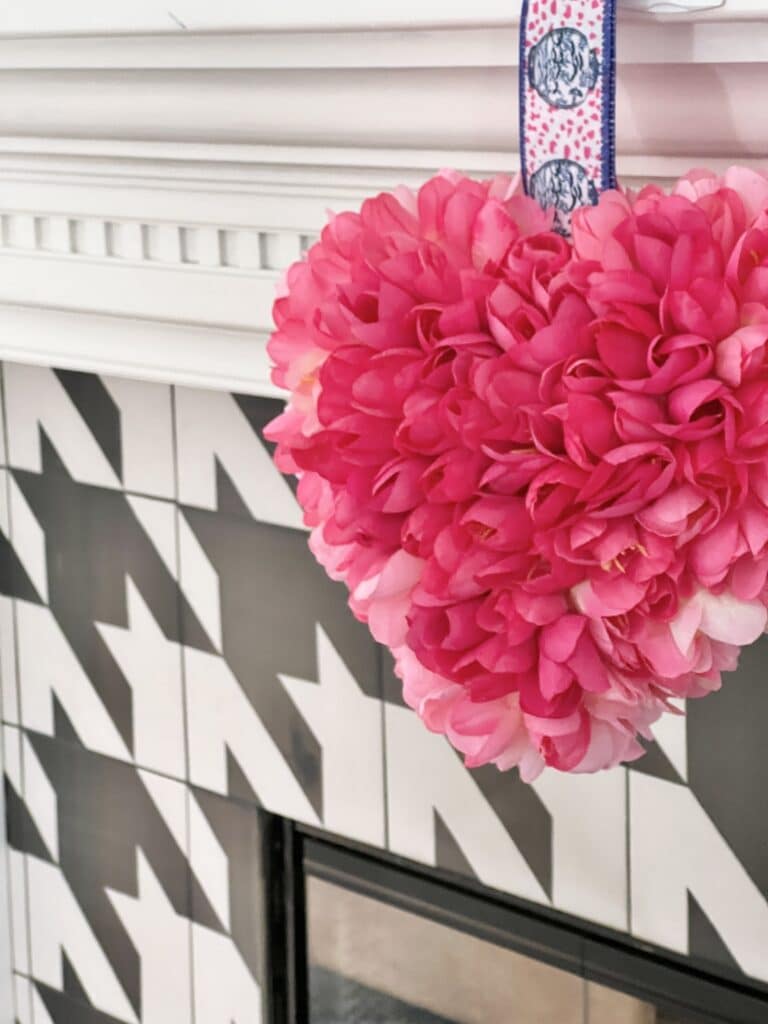 A DIY pink Valentine heart hanging from the fireplace hearth after the maakeover.