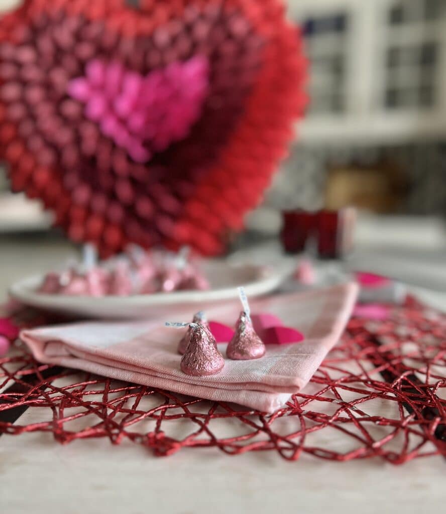 Foil wrapped chocolate kisses sitting in front of a paper cone Valentine heart.