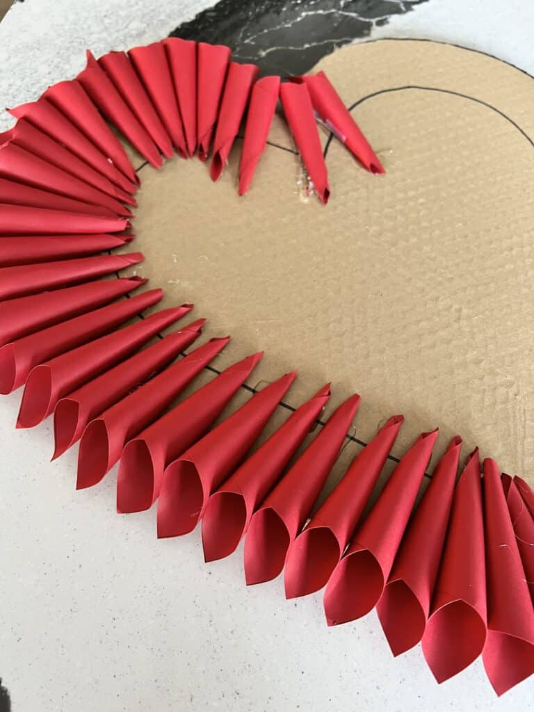 Glueing the paper cones around the perimeter of the cardboard heart.