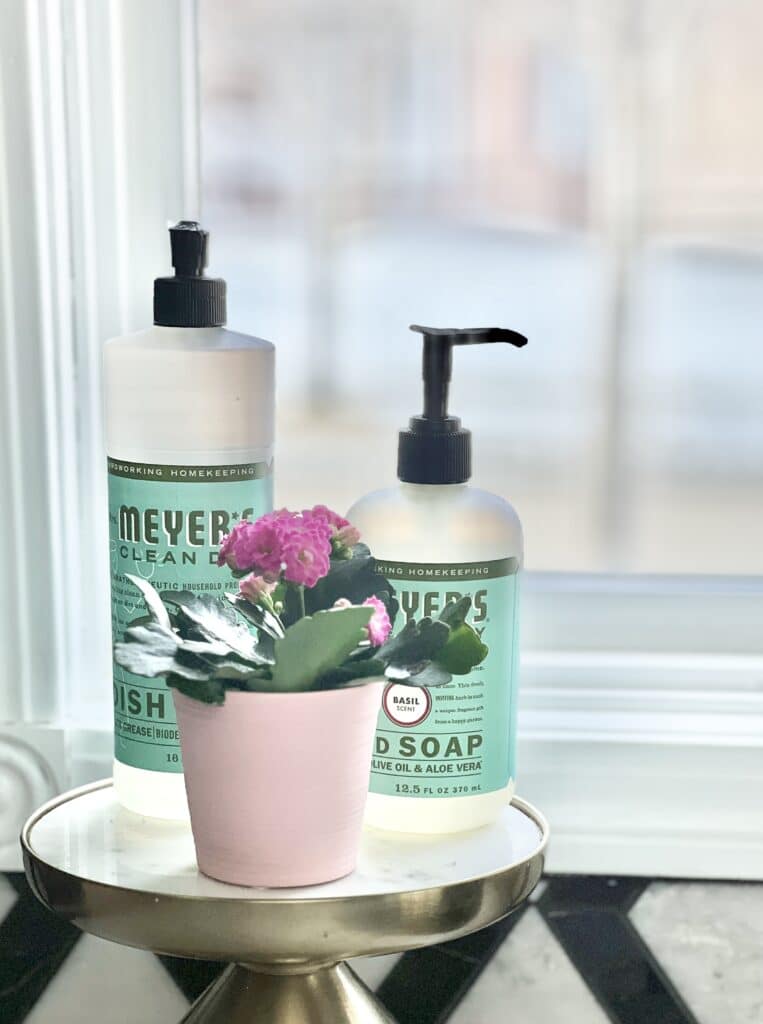 Sweet pink flowers sitting with some dish washing soap and hand soap by the kitchen sink.