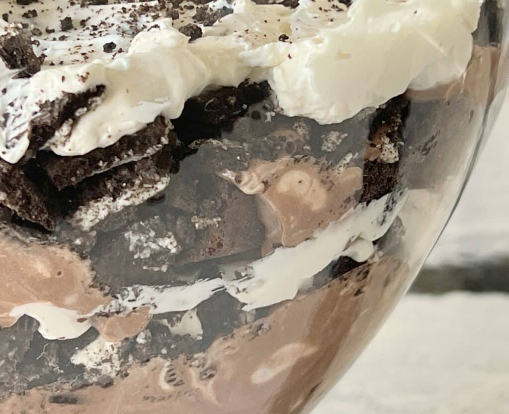 The four intermingling layers of the chocolate trifle include brownies, crushed sandwich cookies, a cream cheese mixture, and a pudding mixture.