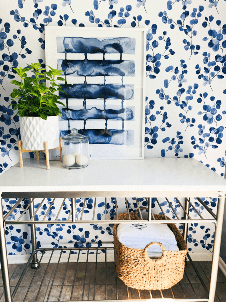 Layered blue and white patterns in wallpaper and wall art in a laundry room.