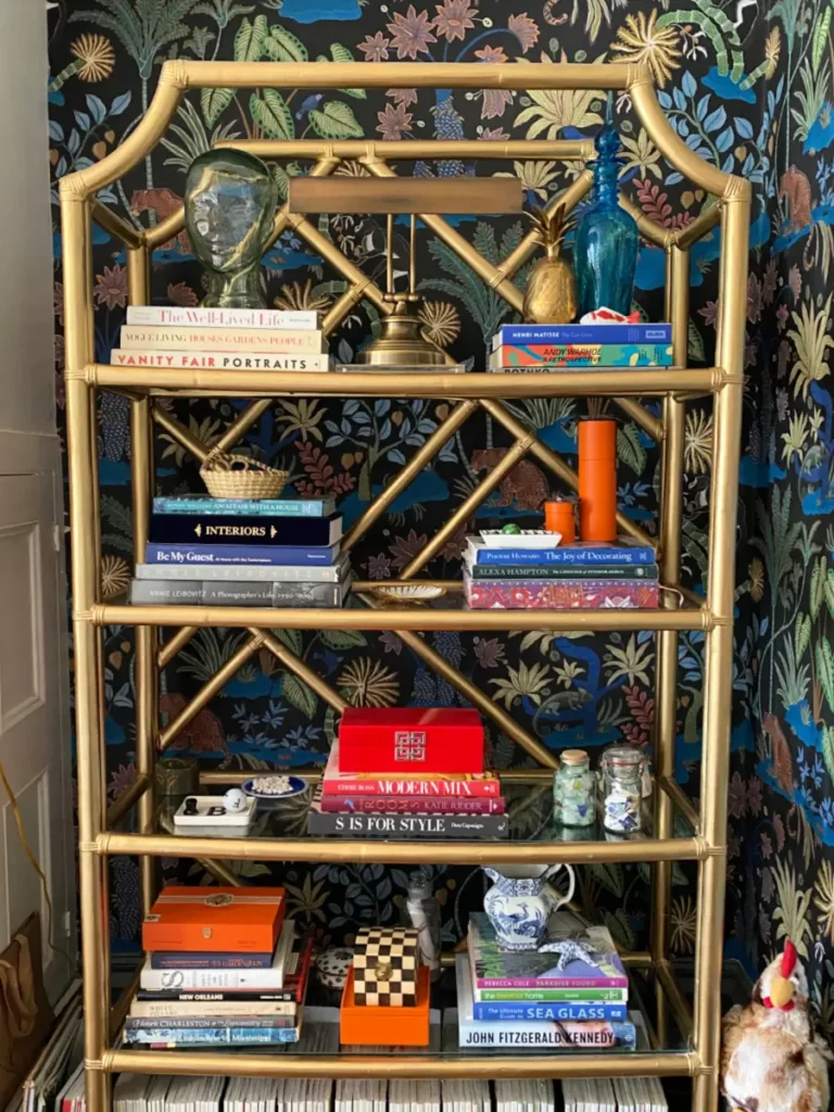 A gold bookcase against a beautiful wallpapered wall.