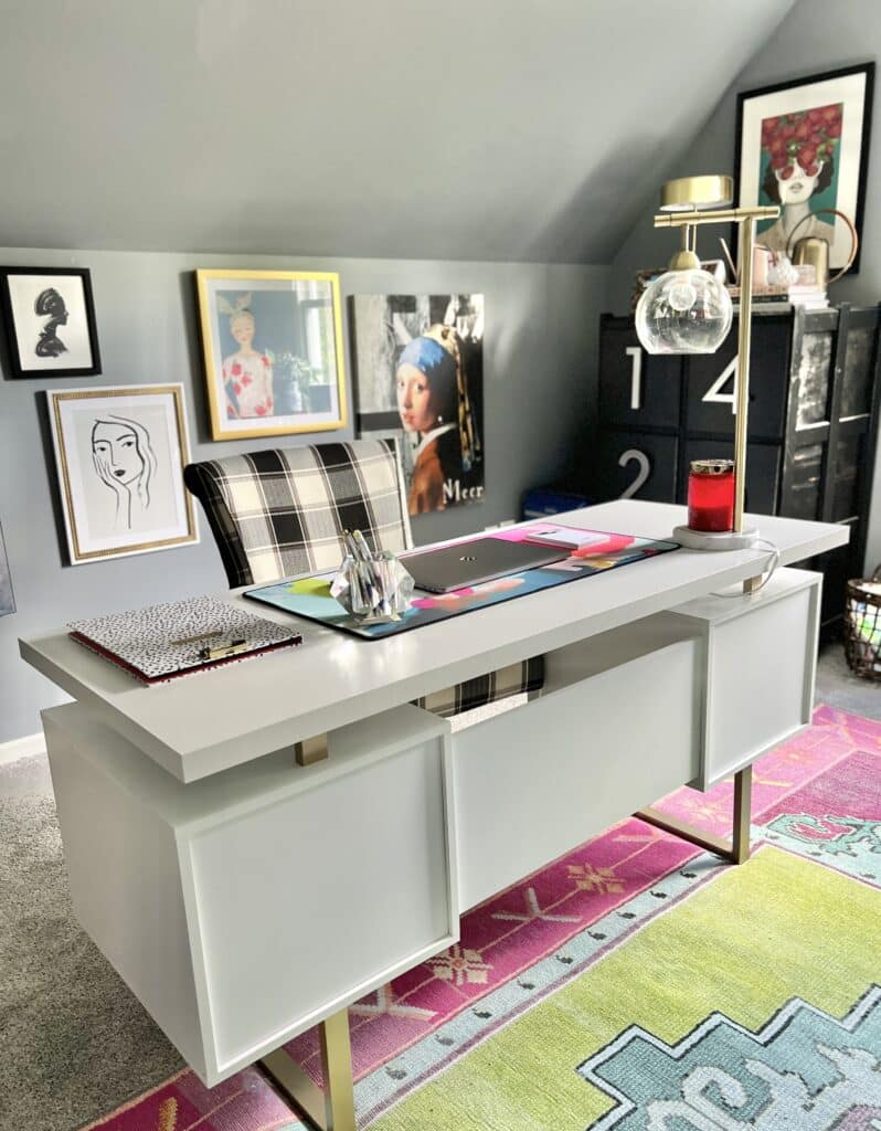 Colorful home decor in a home office include a pink rug, bright wall art and a multi-colored desk blotter.
