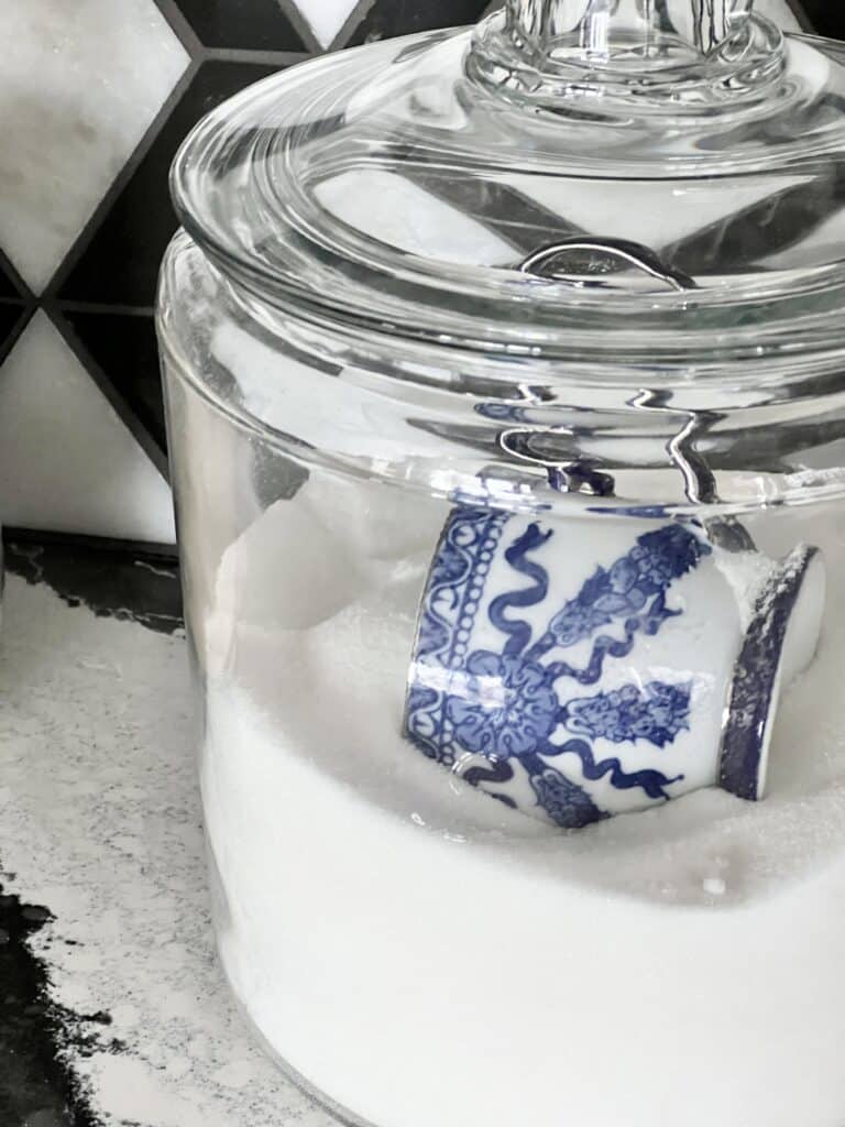 A blue and white teacup is a scoop in a glass sugar canister.