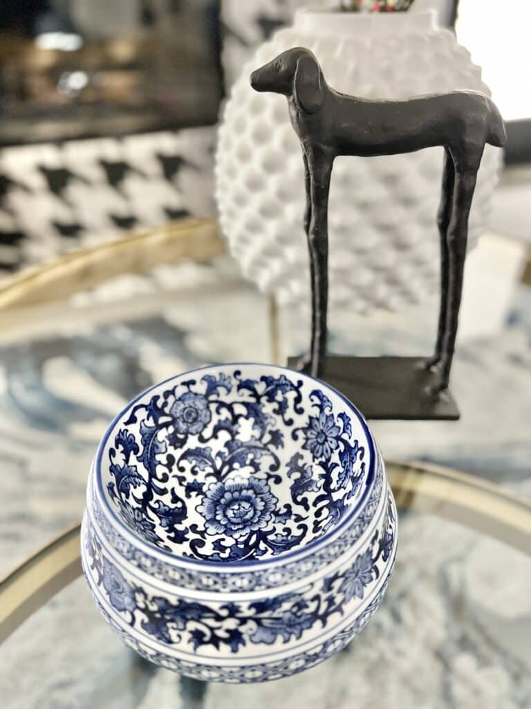 A blue and white dog bowl sitting on a coffee table beside a dog sculpture.