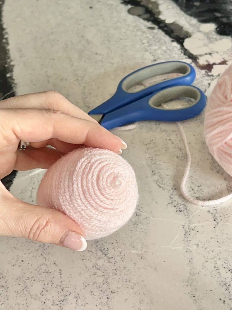 Winding a plastic egg with yarn from top to bottom.