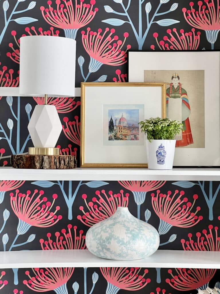 Layered artwork sits on the shelves of the newly painted and wallpapered bookcase.