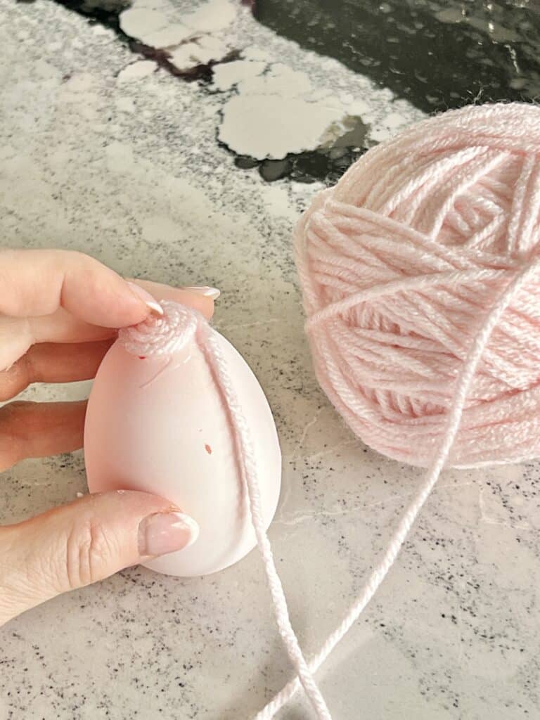 Glueing pink yarn to the top of a plastic egg.