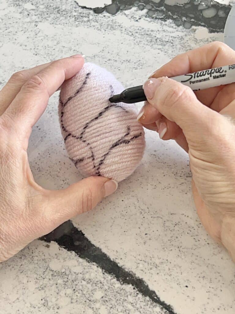Drawing small branches on a yarn wrapped egg.