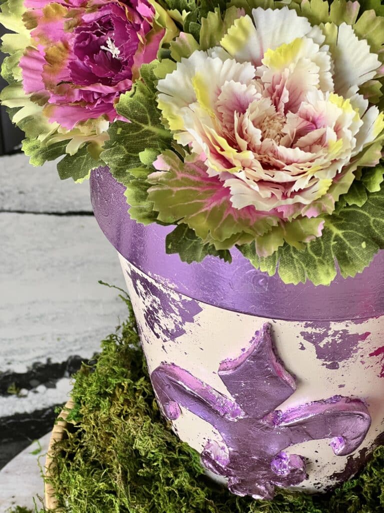 The flower pot embellished with the air dry clay fleur de lis and styled with faux cabbages.