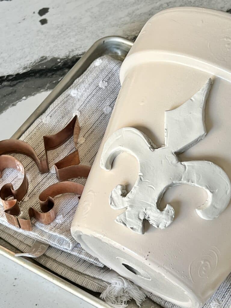 Laying the air dry clay cutout onto the curved side of the terra cotta flower pot.