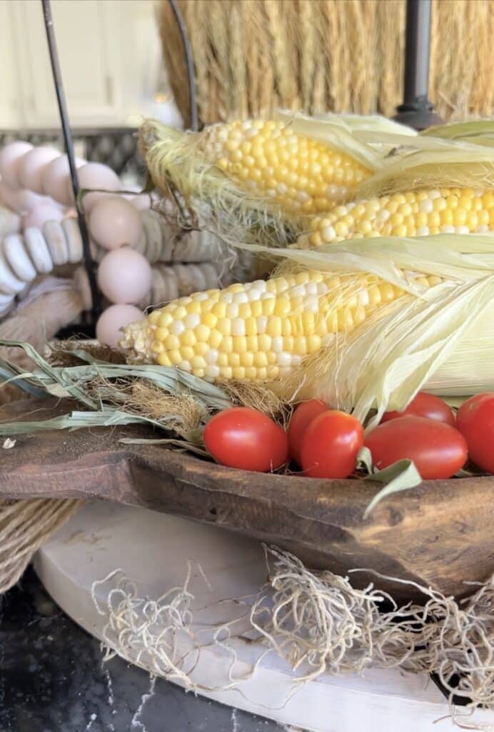 A dough bowl full of bright yellow corn and red tomatoes.