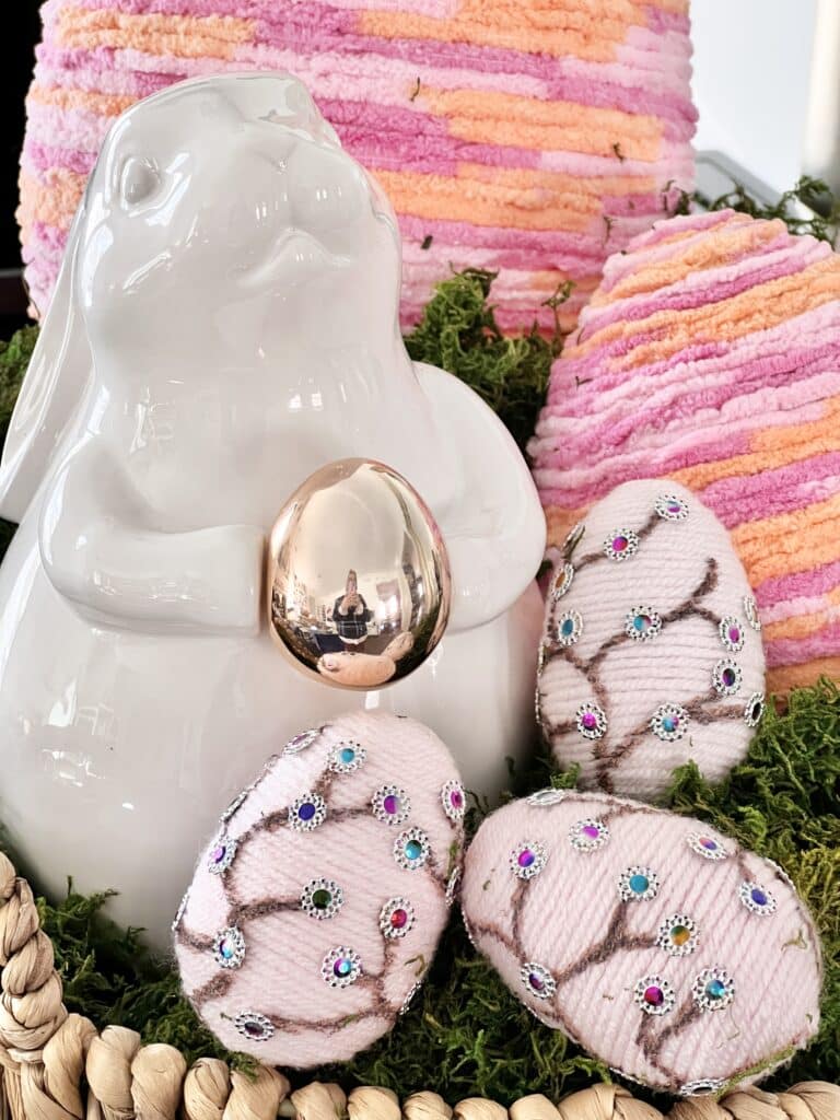 Yarn wrapped decorative eggs displayed beside a white ceramic Eater bunny.
