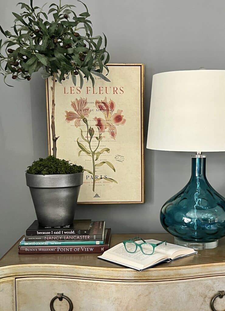 The faux olive topiary tree sitting on a stack of books on a bedroom nightstand.