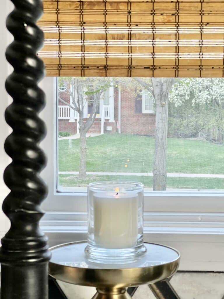 A candle in a jar on a pedestal by the kitchen sink.