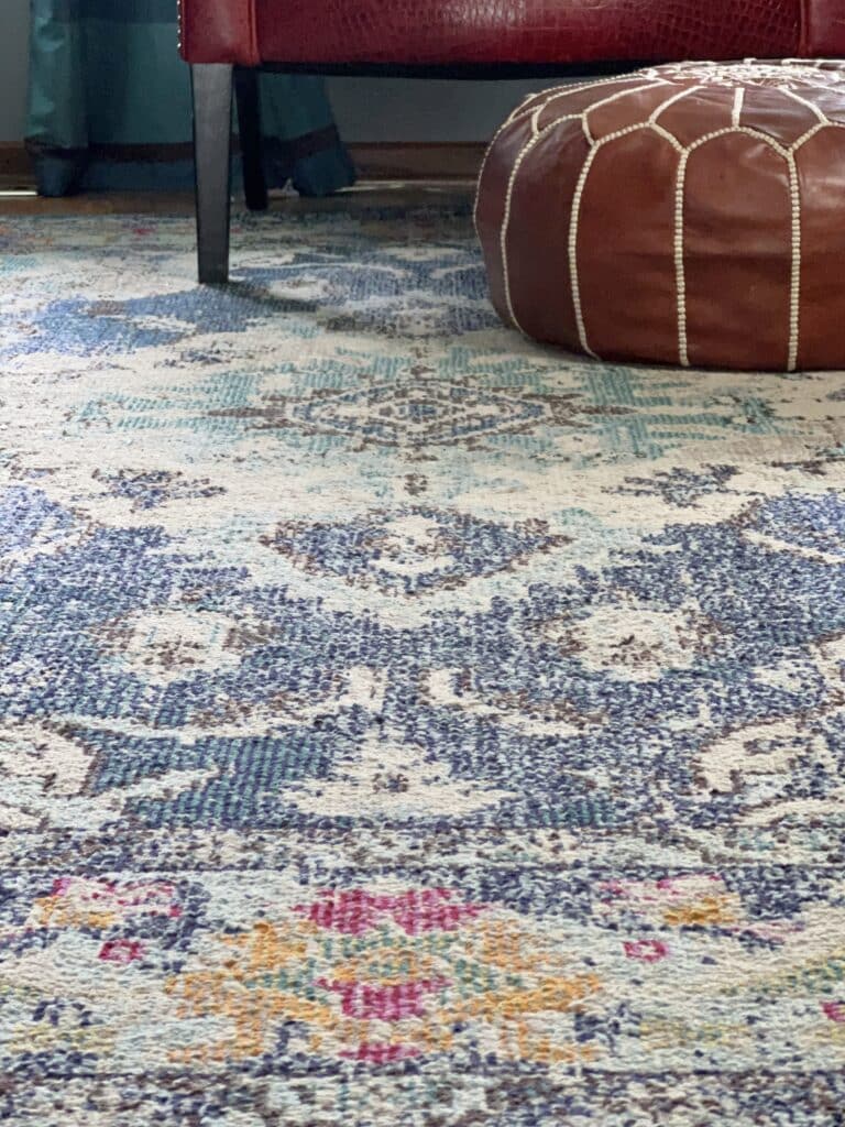 A colorful rug underneath a red chair and brown leather ottoman.