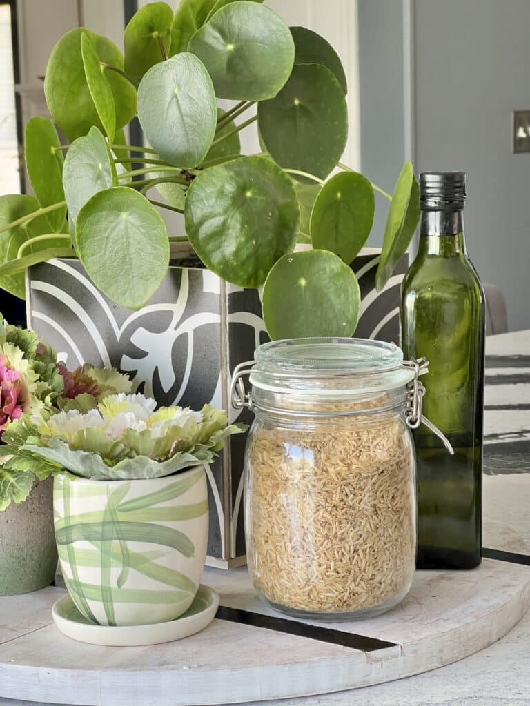 A lidded glass jar containing balsamic rice is displayed on a wooden board with olive olive and plants.