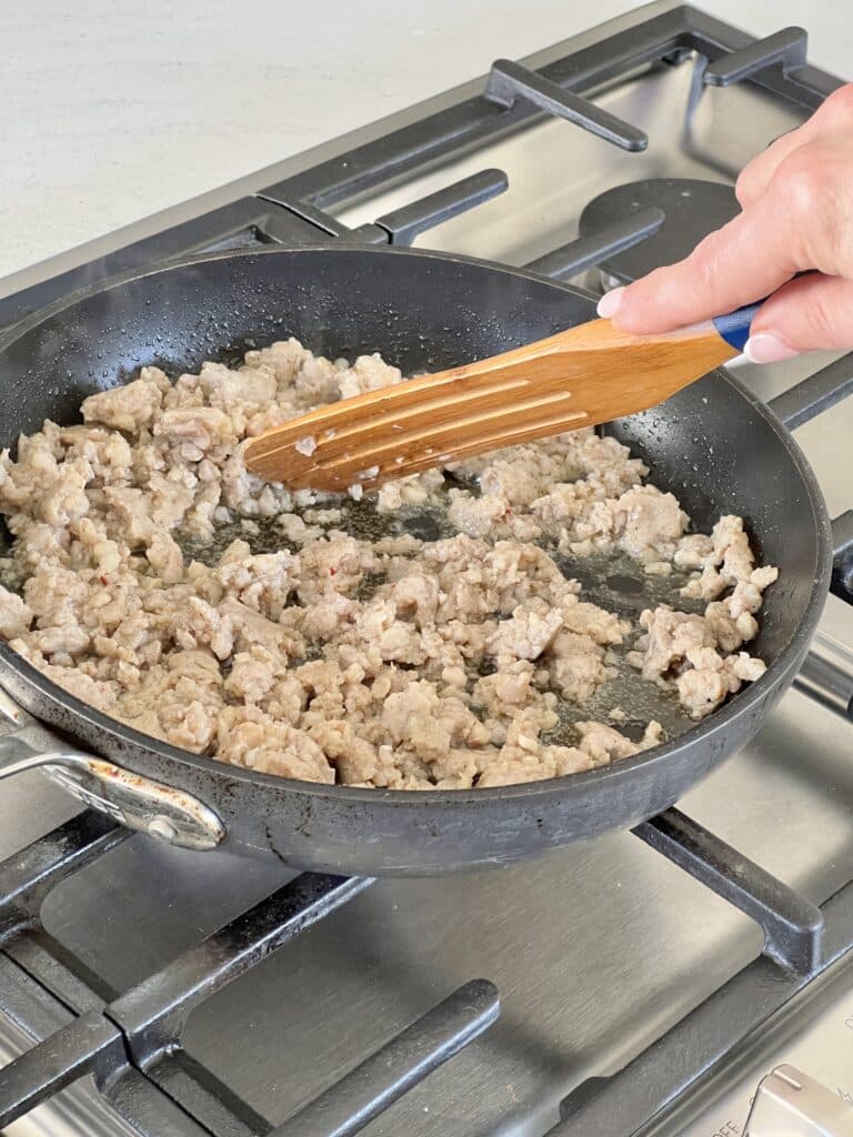 Browning pork sausage in a skillet on a stovetop.