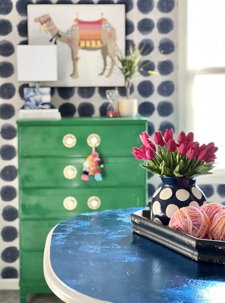 A color blocked craft studio with a green chest, blue table, and blue and white polka dot wallpaper.