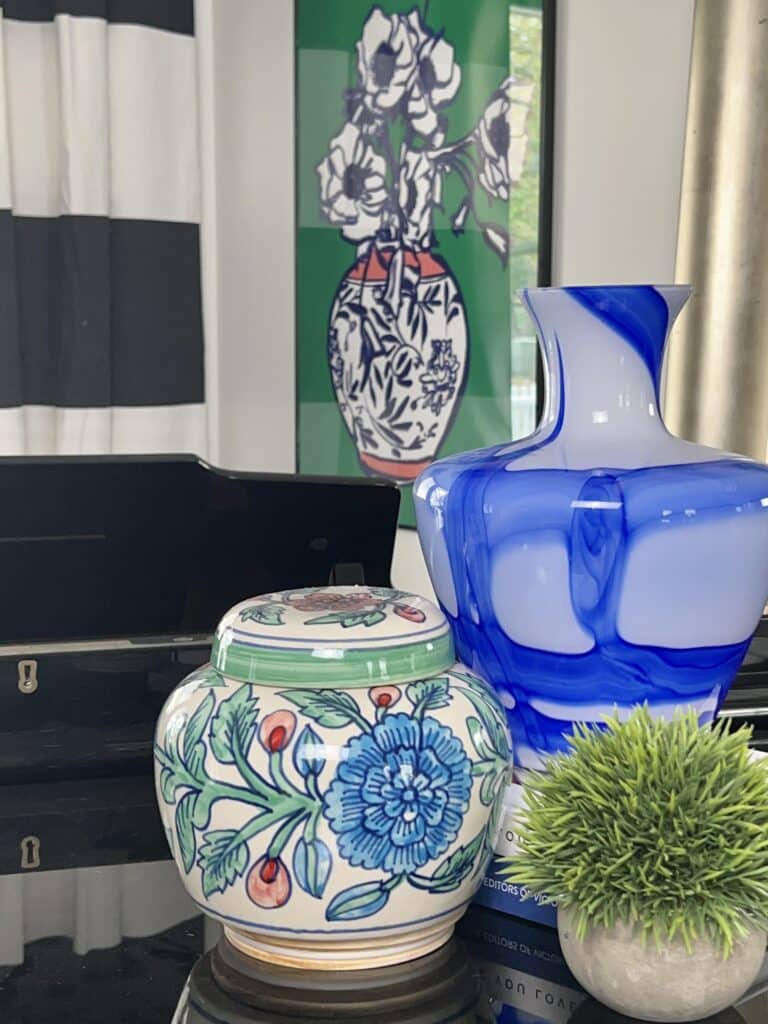 Colorful home decor that includes a blue and white glass vase, a green faux plant, and a multi-colored lidded jar.