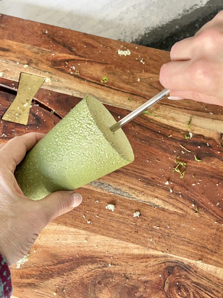 Creating a pilot hole in the bottom of a styrofoam cone with a metal straw.