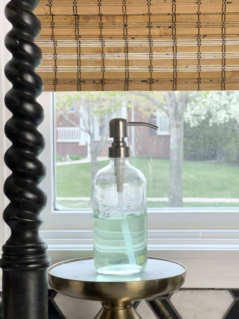 A glass bottle filled with hand sanitizer sitting on a pedestal by the kitchen sink.