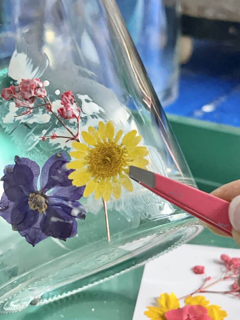 Applying a pressed flower to the side of the bottle vase.